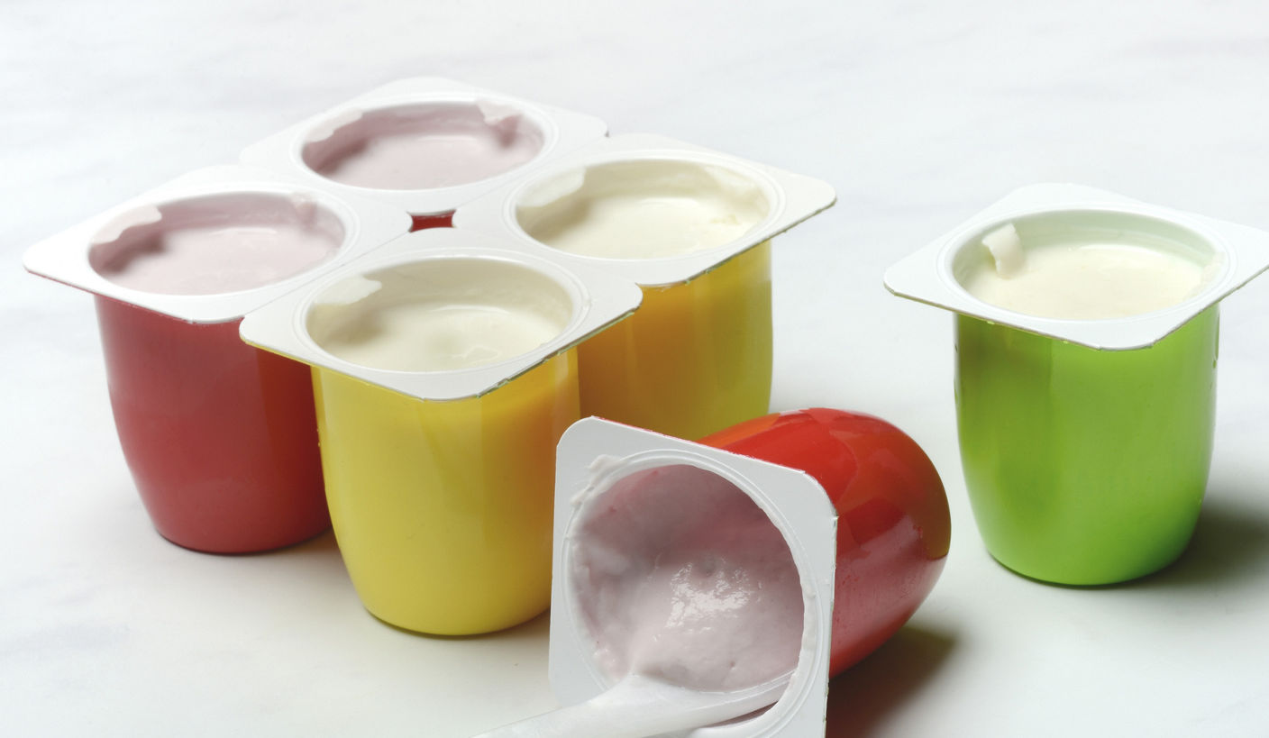 Single-serve yogurt cups in bright red, yellow, and green colors are arranged on a white surface, with one open cup and spoon