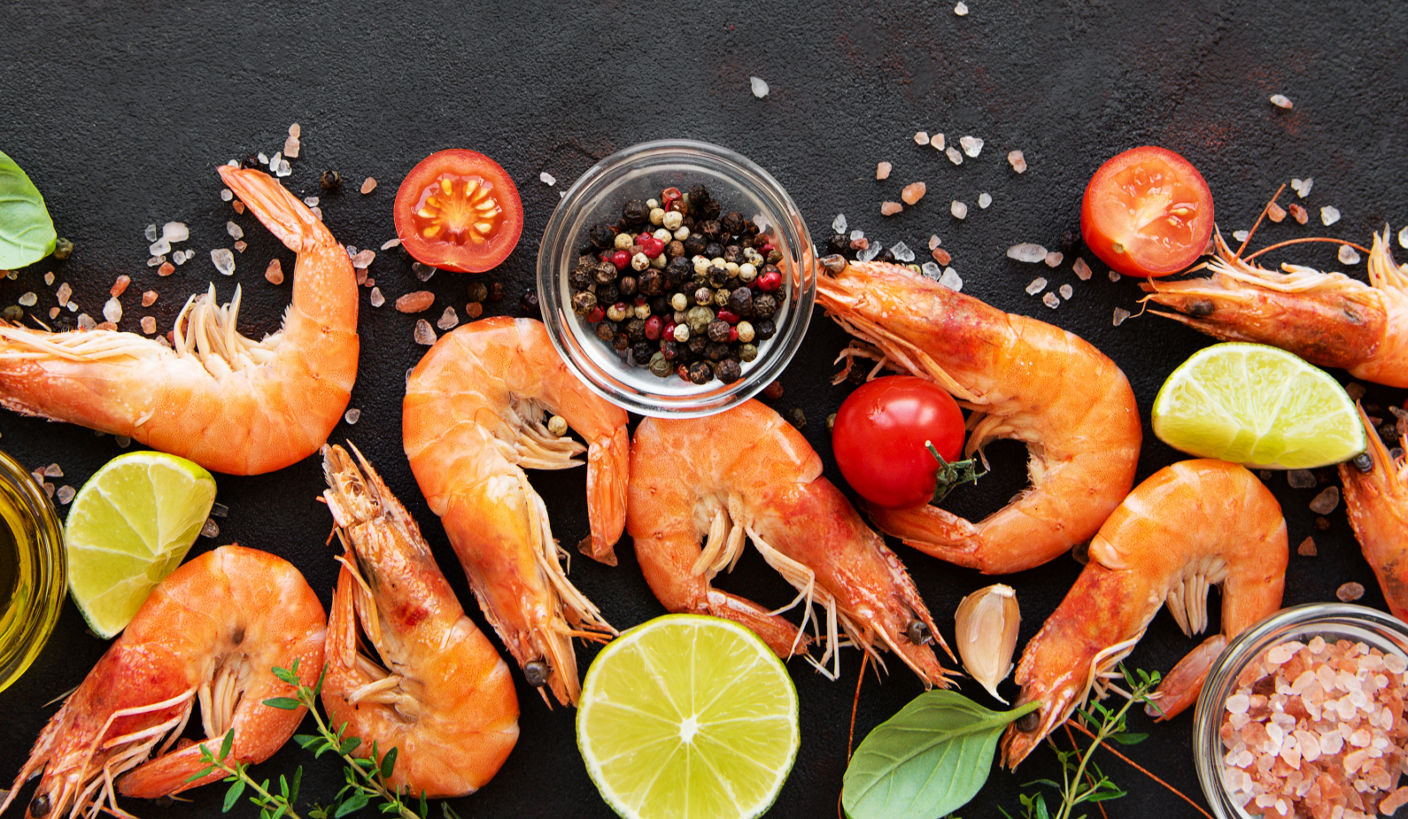 A vibrant culinary arrangement featuring cooked shrimp, halved cherry tomatoes, lime wedges, and fresh basil leaves, artfully placed on a dark surface. 