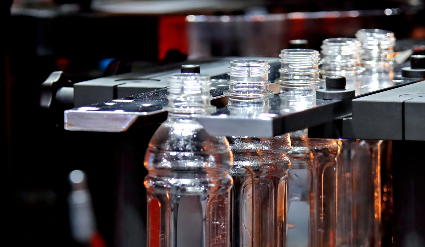Row of clear plastic bottles held in a metal fixture on an automated manufacturing line