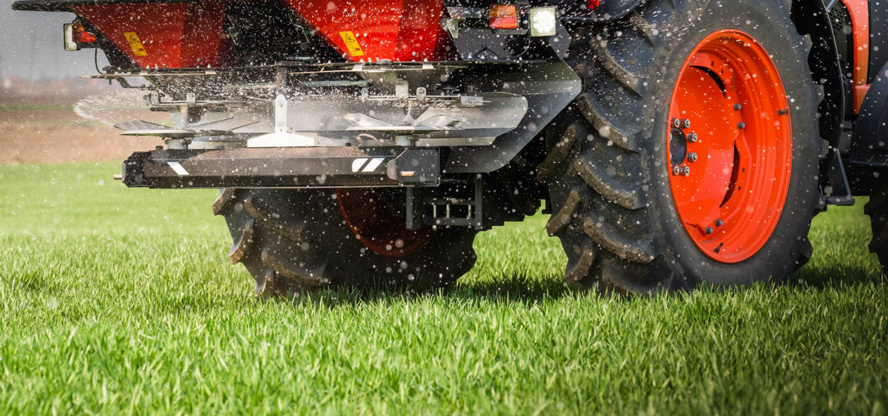 Close-up of a tractor with large wheels dispersing fertilizer across a vibrant green field