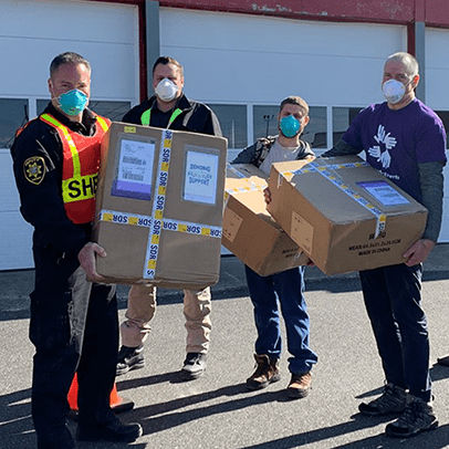 A group of four men with masks on holding shipping boxes